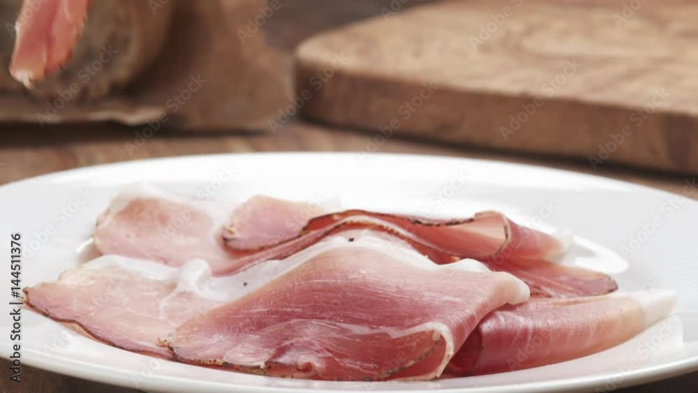 Slow motion of Italian speck ham falling on white plate closeup, 180fps prores footage Slow motion of Italian speck ham falling on white plate closeup, 180fps prores footage