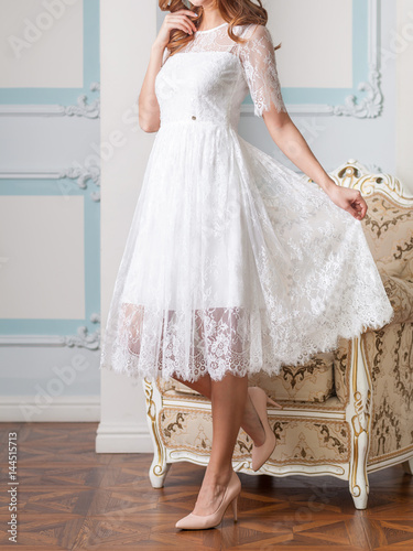 Attractive blond woman in white lace dress with beautiful long hair posing against the expensive antique armchair