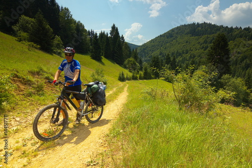 A tourist with a bicycle on a way with mountain meadows