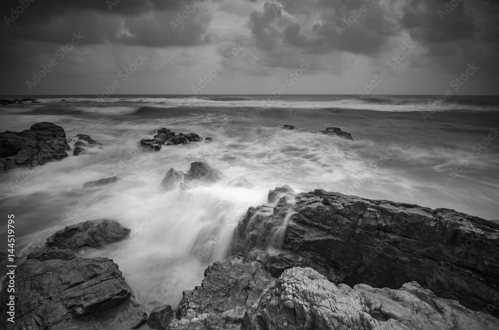 Black and white image, beautiful nature wave hitting the rock over dramatic cloudy sky