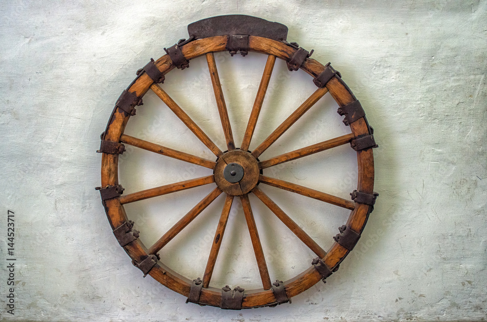 Old wagon wheel. Vintage wood-metal wagon wheel on white wall.