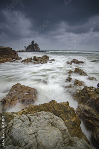 beautiful beach with rock hitting by waves. soft focus due to long exposure. dramatic dark clouds and rocky island