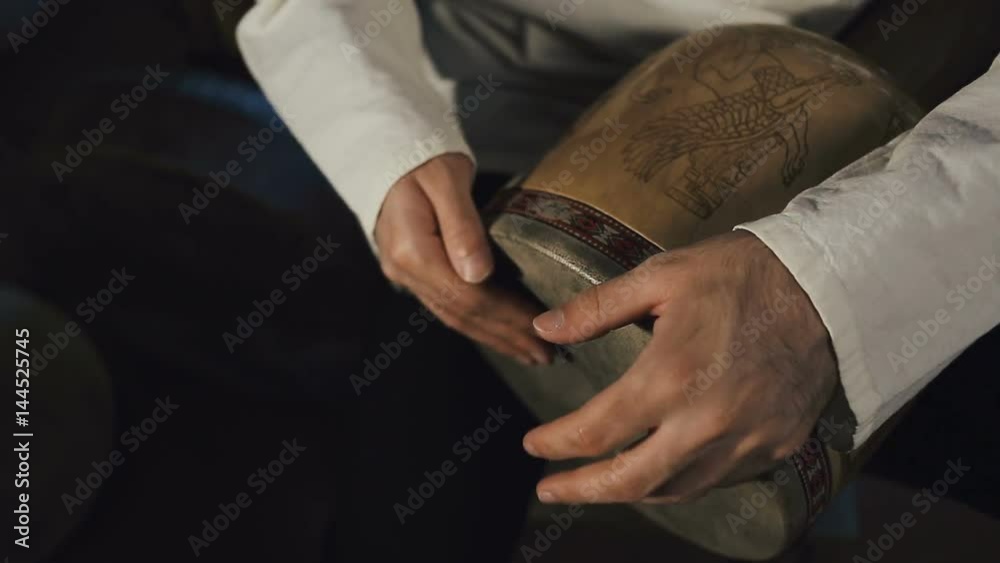 close up panoramic shot of man's hands drumming out a beat on an arabic percussion drum named Tombak at home. Shot with other percussian drums on background.