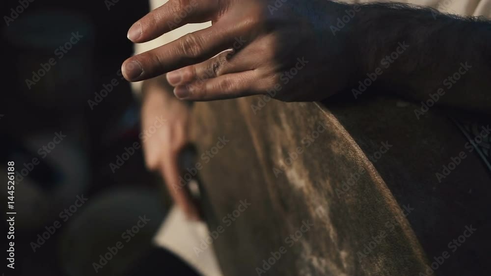 close up shot of man's hands drumming out a beat on an arabic percussion drum named Bendir at home. Shot with other percussian drums on background.