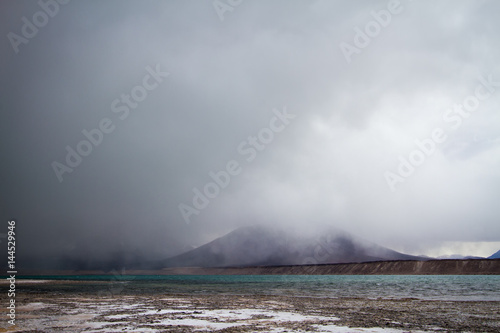 Green lagoon with low clouds next to a volcano, on the border between Chile and Argentina