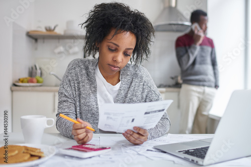 Slika na platnu African american female reading piece of paper, calculating gas and electricity