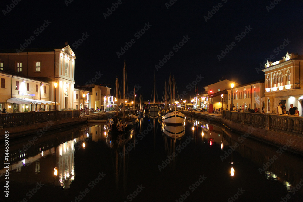 Italy. Emilia-Romagna. Cesenatico. Canal with ship on black sky background horizontal view. Night.