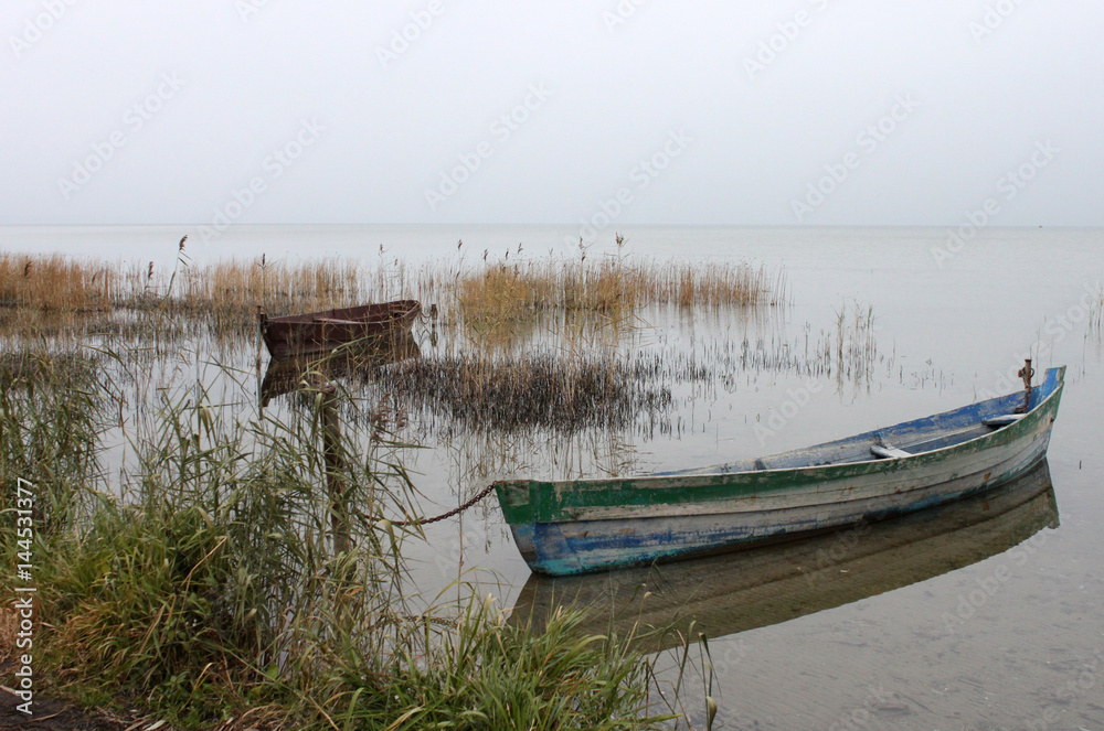 Two boats in the lake in the cloudy weather on gray sky background, horizontal view. Two boats in the lake in the cloudy weather on gray sky background, horizontal view.