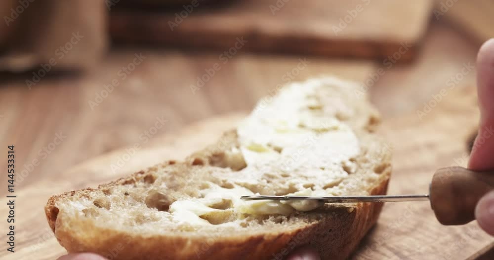Slow motion of female teen hand spreads butter on slice of rustic bread, 4k 60fps prores footage