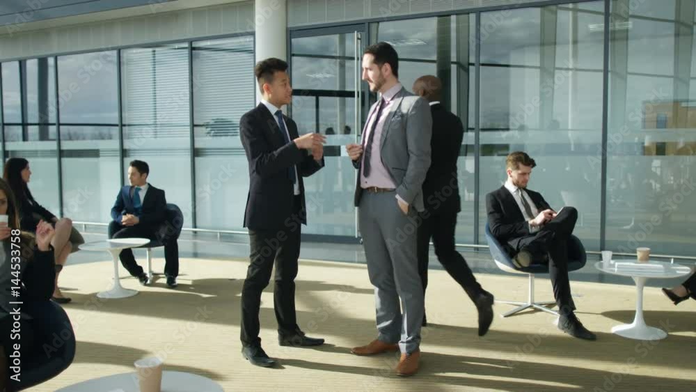 Businessmen having a conversation in crowded area of large modern office Businessmen having a conversation in crowded area of large modern office