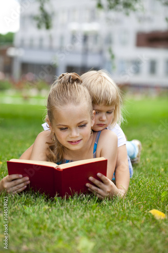 Adorable cute little girl reading book outside on grass