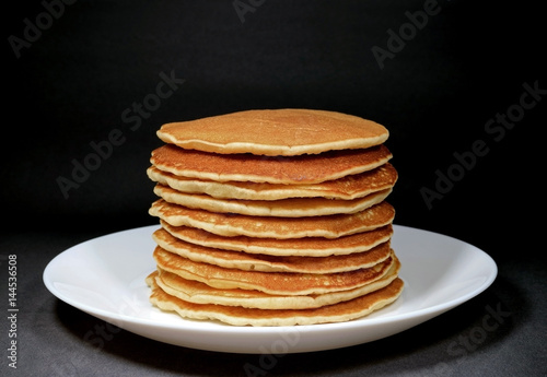 Piled up homemade plain pancakes served on white plate, isolated on black background 