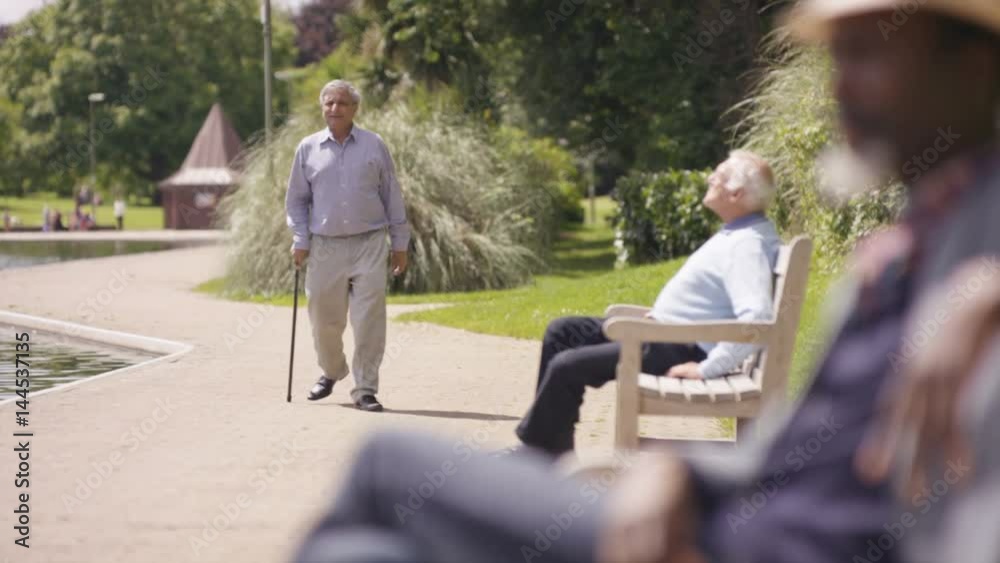  Senior man greeting a friend in the park & sitting down for a chat