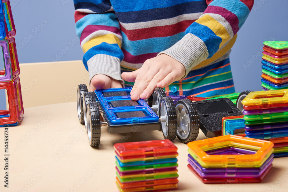 Kid playing toy magnetic construction set. He is crafting a car.
