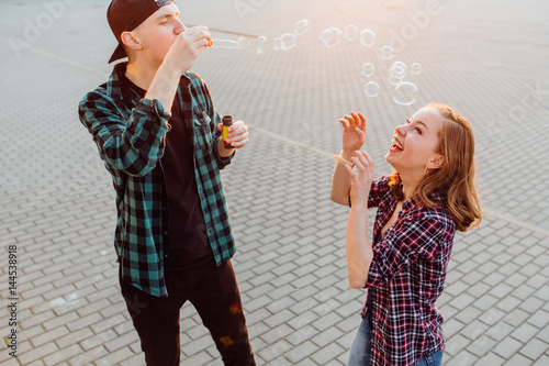 Young pretty woman and young hipster boy blowing bubblesand heaving fun in summer time. photo