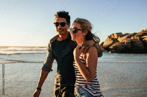 Young happy couple walking on seashore and smiling.