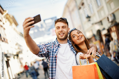 Attractive young couple doing selfi after shopping in downtown