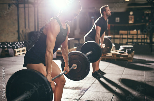 Fit man and woman deadlifting heavy barbells