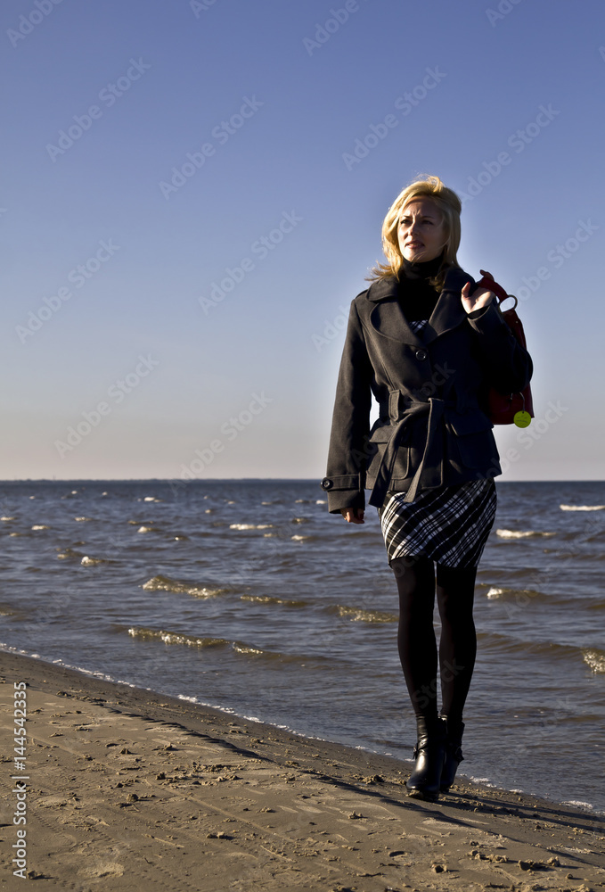 Portrait of blond and attractive woman walking along the sandy beach on sunny day.