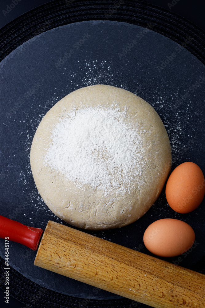 Homemade organic Dough whit rolling pin and eggs for bake pizza or bread on black slate stone plate Homemade organic Dough whit rolling pin and eggs for bake pizza or bread on black slate stone plate