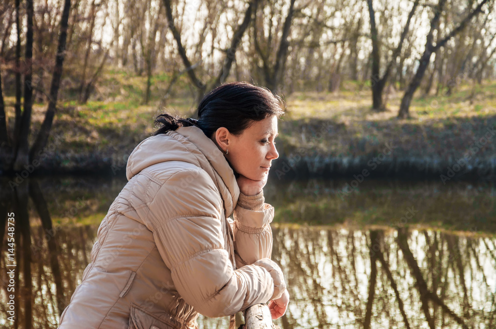 Girl dreams of sitting on a bridge with a forest and river in the background. Girl sitting on a pier and looking at the river..a blurred background Girl dreams of sitting on a bridge with a forest and river in the background. Girl sitting on a pier and looking at the river..a blurred background