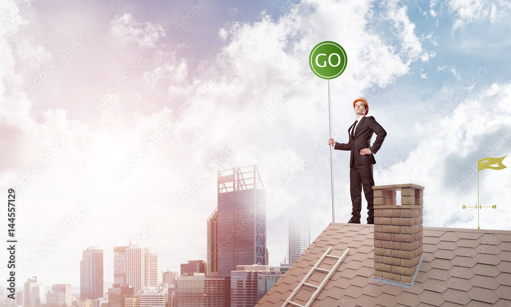Businessman in suit on house top with ecology concept signboard. Mixed media Businessman in suit on house top with ecology concept signboard. Mixed media