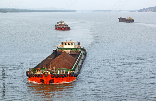 Large cargo barges transporting iron ore mined in hinterland to the main harbor for loading into big ships for exporting, along Mandovi River in Goa, India