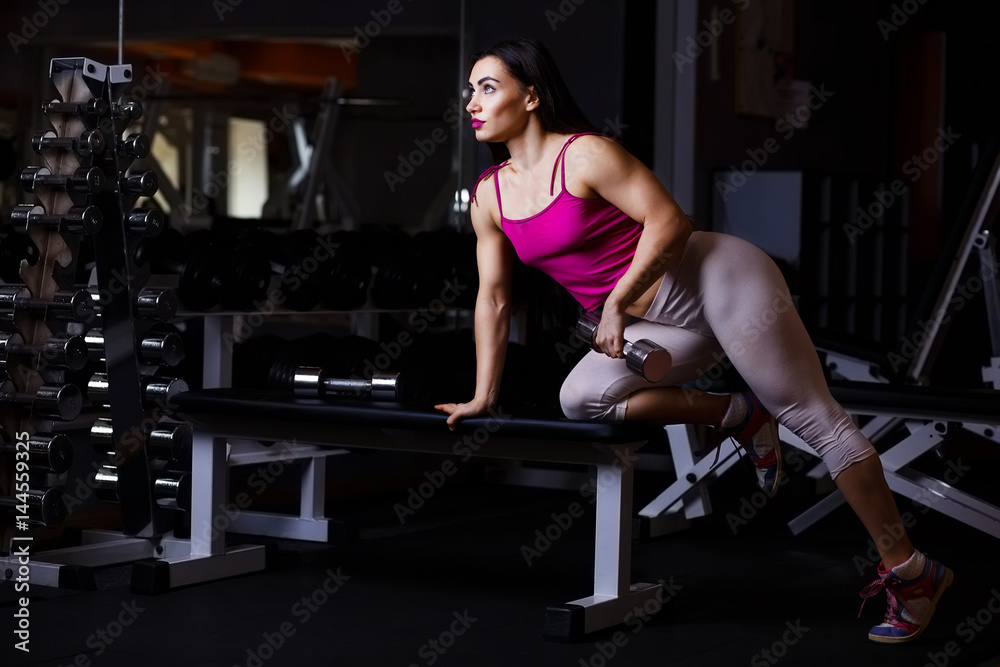 Fototapeta premium Young attractive muscular fitness woman doing exercise with dumbbell in gym