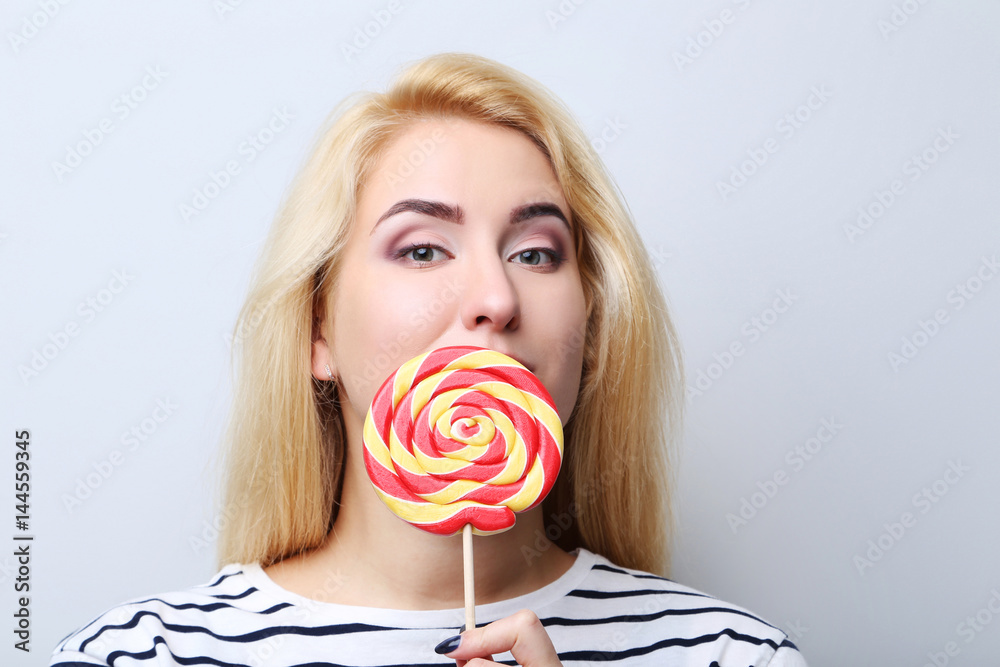 Young beautiful woman with lollipop on grey background