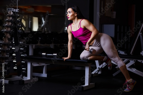 Young attractive muscular fitness woman doing exercise with dumbbell in gym