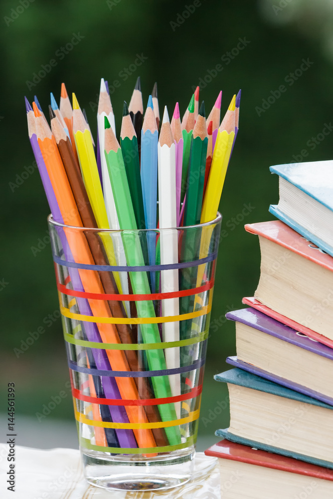 Fototapeta premium Heap of colored pencils in a glass, books.