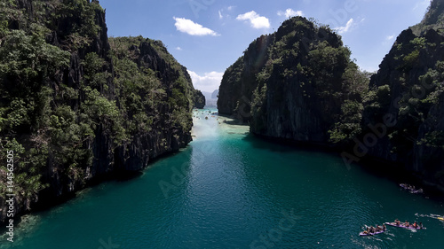 A view from above of a small lagoon in which kayaks are floating. Aerial view of the turquoise water between the black steep cliffs.