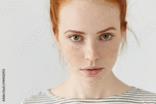 Close up highly-detailed picture of beautiful charming young female with perfect freckled skin, ginger hair and green eyes resting indoors, dressed in sailor t-shirt. Teenage girl posing in studio photo