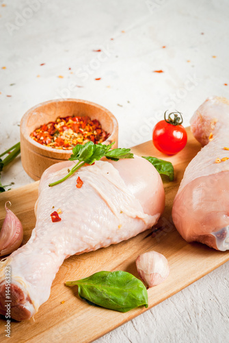 Raw chicken legs. Meat, a source of protein. On a cutting board, on a white stone table. With spices, herbs and tomatoes for cooking. Top view copy space
