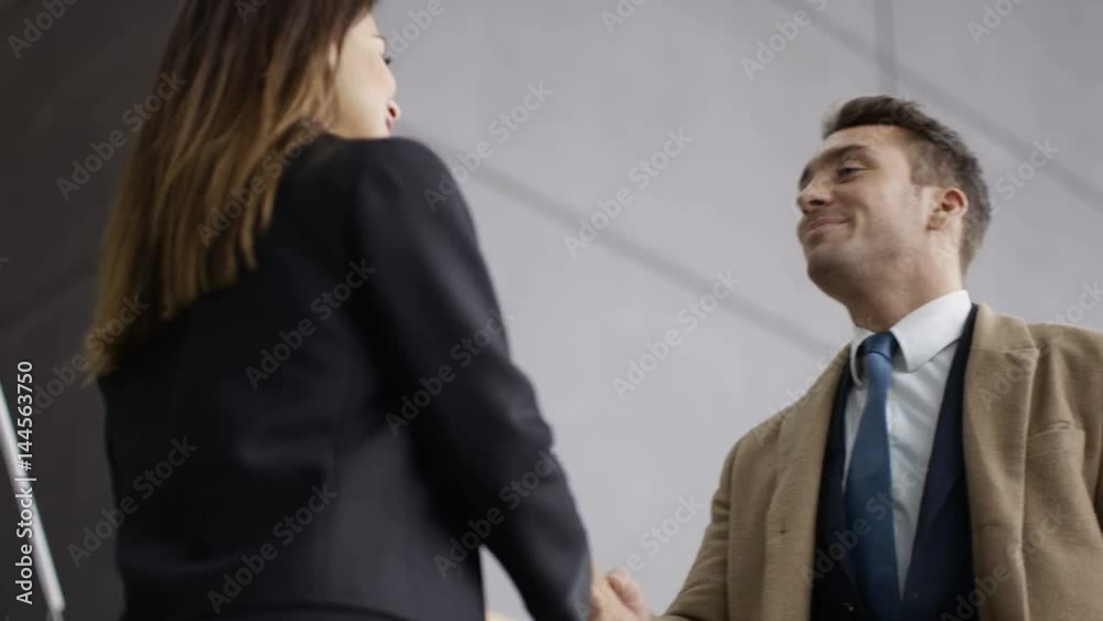 Business man & woman meet & shake hands in lobby area of modern office Business man & woman meet & shake hands in lobby area of modern office
