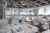 white daily interior of the restaurant with panoramic windows and wooden walls. White tablecloths with gilding. Served tables with wine glasses