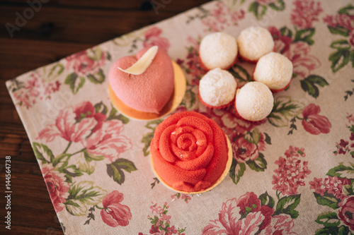 Different cakes on a wooden table and rag napkin in flowers. Red cakes.