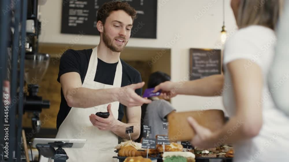  Cheerful worker serving customers & taking payment in city coffee shop