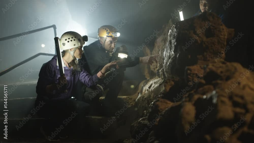 Team of potholers with hard hats and lamps exploring underground cave system Team of potholers with hard hats and lamps exploring underground cave system