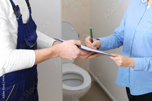 Female customer signing contract with plumber indoors © Africa Studio