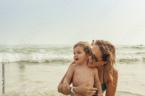Woman and baby boy having a bath in the seashore of the beach. Summertime.