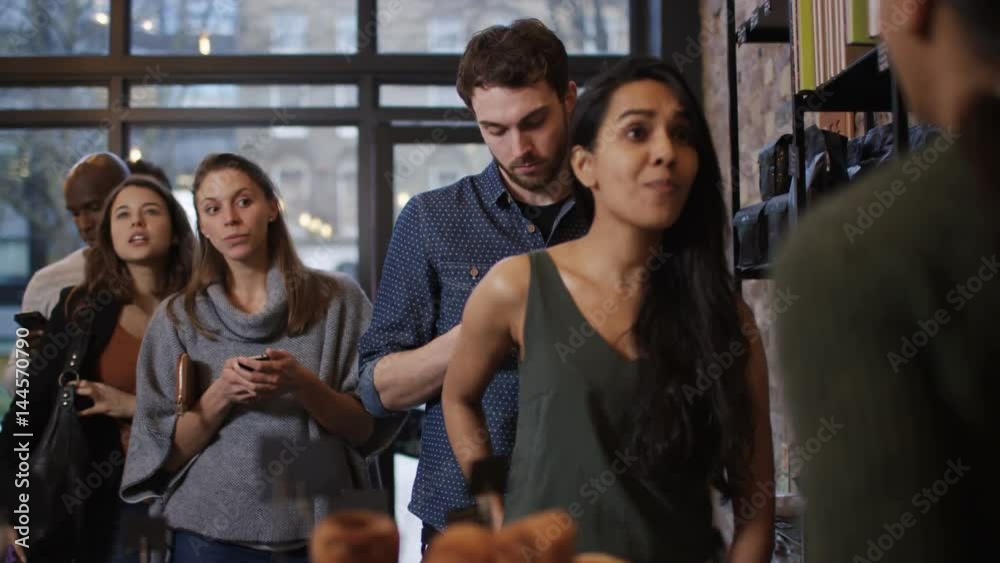  Customer in cafe makes payment with smartphone while queue of customers wait 