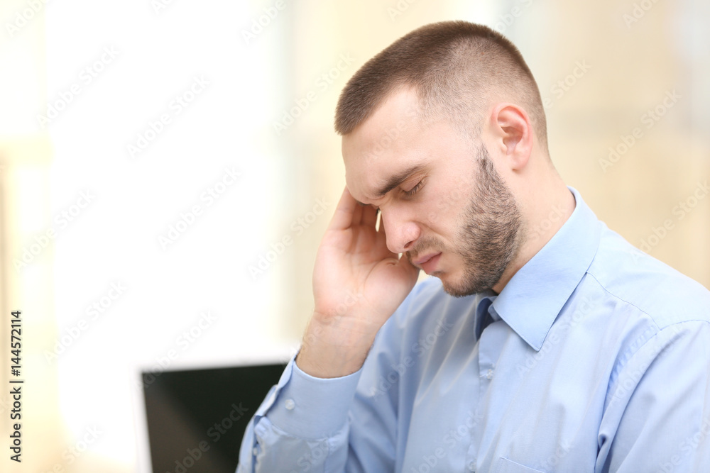 Handsome young man suffering from headache while working in office