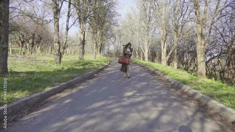 Girl with a book in her hands is walking along the avenue of a spring park, slow motion Girl with a book in her hands is walking along the avenue of a spring park, slow motion