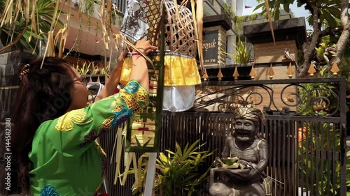 Balinese woman in traditional ceremony costume decorating penjor on Galungan day (Bali holiday ceremony). Medium shot with Sony a7s on tripod on sunny day photo