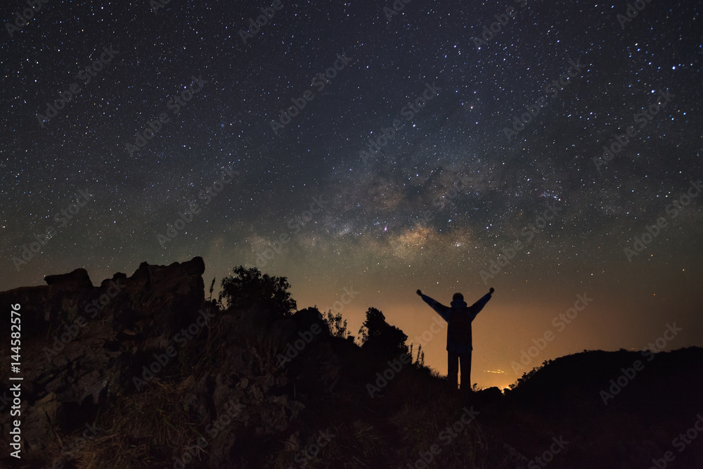 Milky way galaxy and silhouette of a standing happy man at Doi Luang Chiang Dao with Thai Language top point signs. Long exposure photograph.With grain