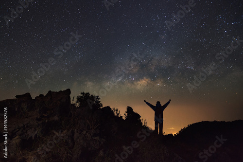 Milky way galaxy and silhouette of a standing happy man at Doi Luang Chiang Dao with Thai Language top point signs. Long exposure photograph.With grain