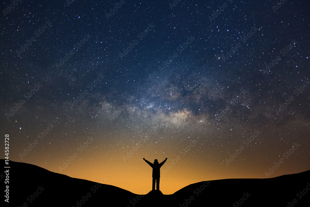 Naklejka premium Milky way galaxy with stars and silhouette of a standing happy man, Long exposure photograph, with grain.