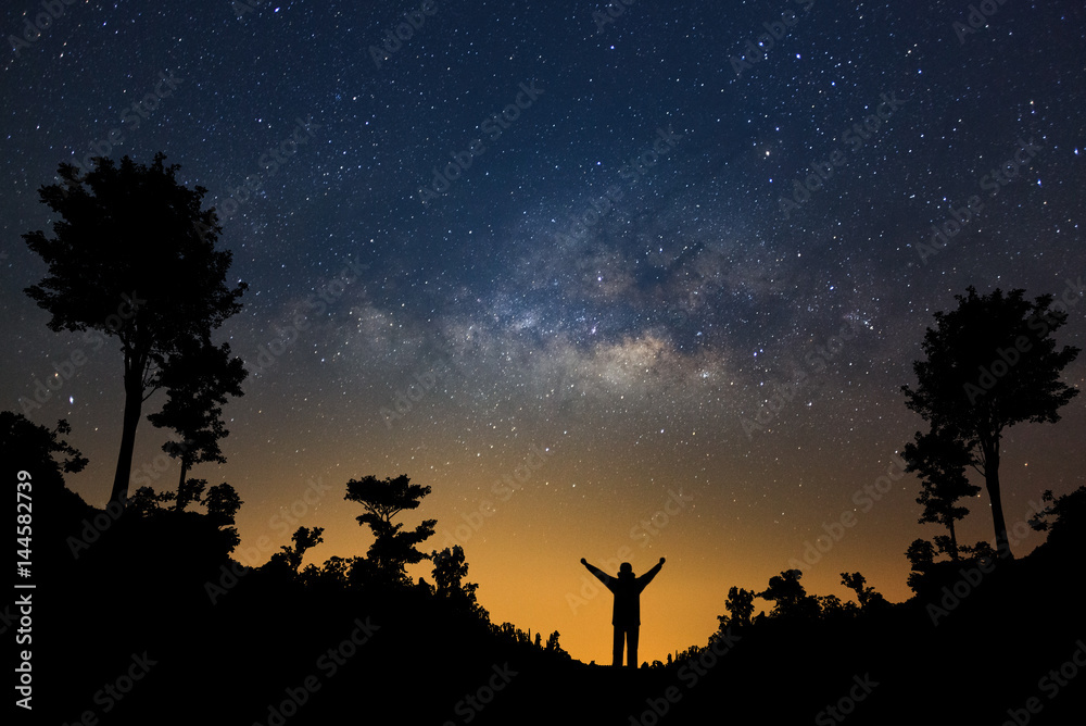 Milky way galaxy and silhouette of a standing happy man in forest, Long exposure photograph, with grain.