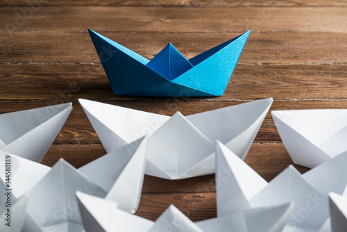 Business leadership concept with white and color paper boats on wooden table